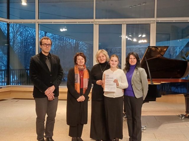 laureāte kopā ar skolotāju Vitu Ramati un zūrijas locekļiem pie klavierēm