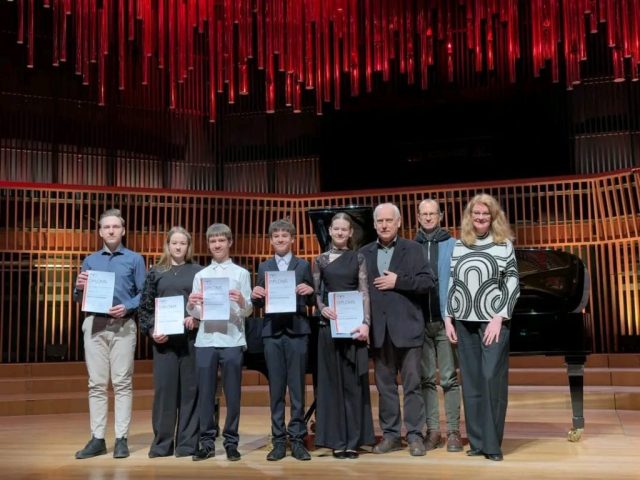 konkursa laureāti sastājušies rindā ar diplomiem rokā pie flīģeļa uz skatuves